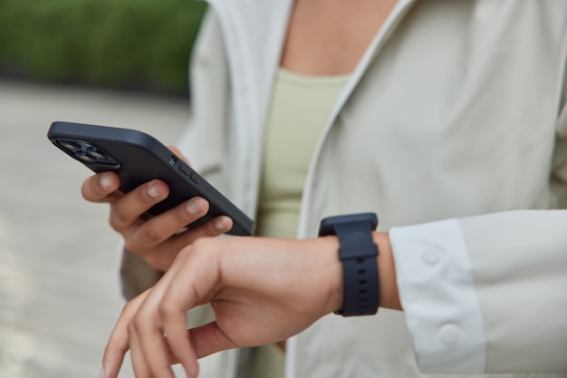 женщина держит современный смартфон и носимые умные часы, используя фитнес-приложение на носимом устройстве, чтобы отслеживать результативность тренировки