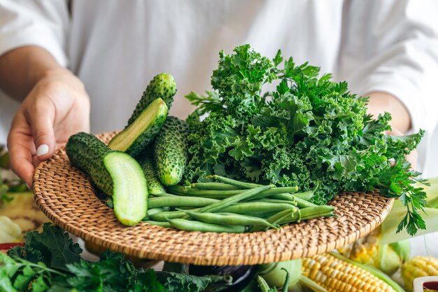 A woman holds a plate with cucumbers kale parsley and green beans closeup