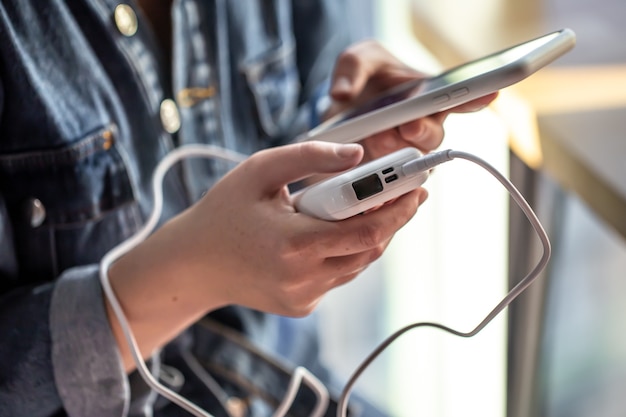 A woman holds a power bank and a phone in her hands, charges the phone from a power bank.