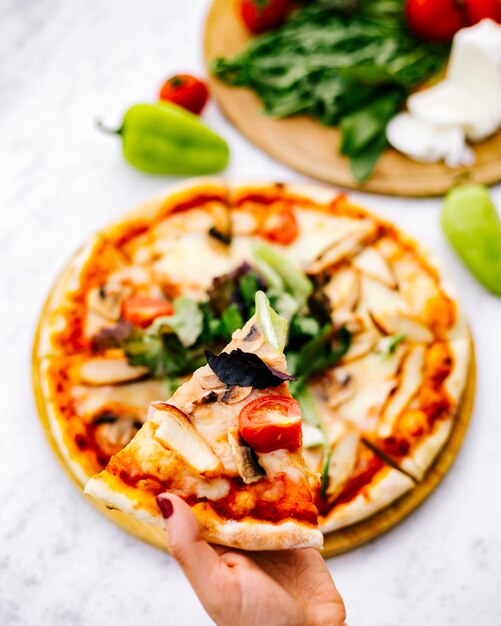 Woman holds a slice of chicken pizza with mushroom tomato topped with herbs