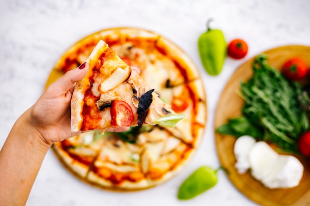 Woman holds a slice of chicken pizza with mushroom tomato topped with herbs
