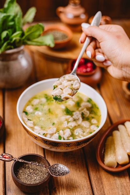 Woman holds a spoon of dushbara dumpling soup served with dried herbs and spices