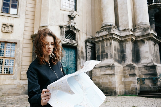 Woman holds touristic map in her arm standing before old cathedral