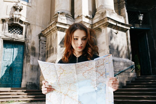 Woman holds touristic map in her arm standing before old cathedral