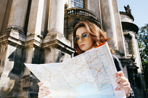 Woman holds touristic map in her arm standing before old cathedral