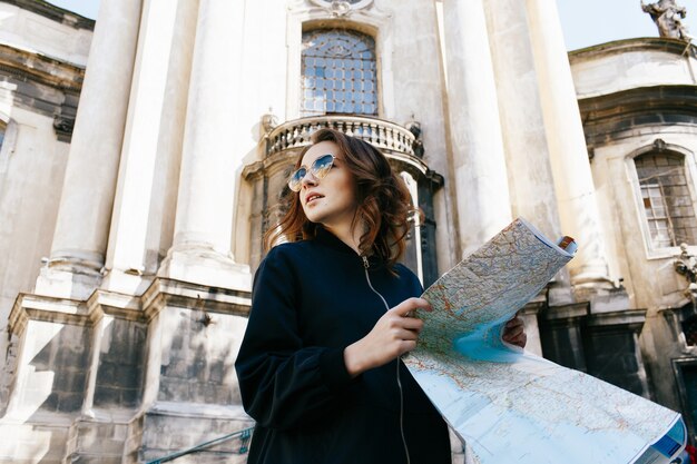 Woman holds touristic map in her arm standing before old cathedral