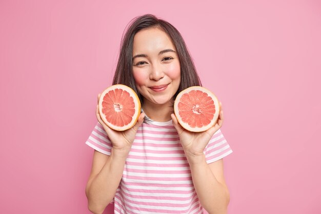 woman holds two halves of grapefruit eats citrus fruit for getting vitamins going to make juice keeps to healthy diet wears striped t shirt 