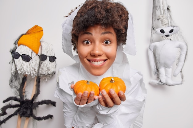 woman holds two small pumpkins prepares decorations for halloween holiday smiles happily poses on white with creepy creatures around