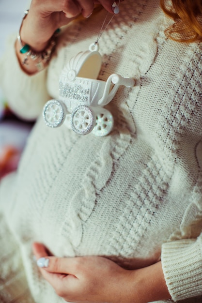 Woman holds white toy carriage on her pregnant belly