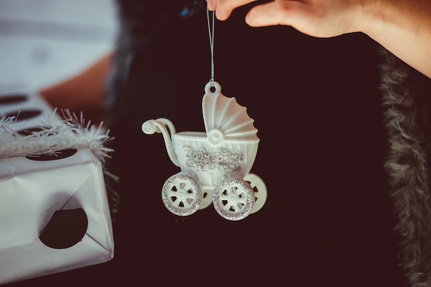 Woman holds white toy carriage on her pregnant belly