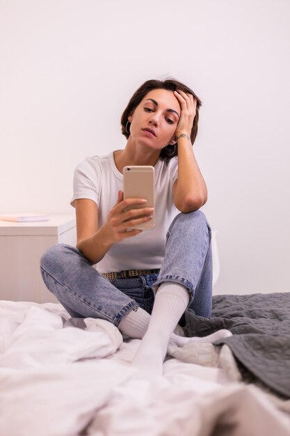 Woman at home in casual clothes cozy bedroom takes photo selfie on mobile phone in mirror