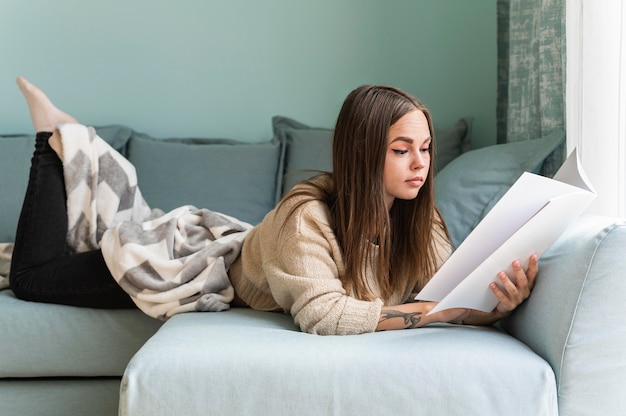 Женщина дома на диване читает книгу во время пандемии