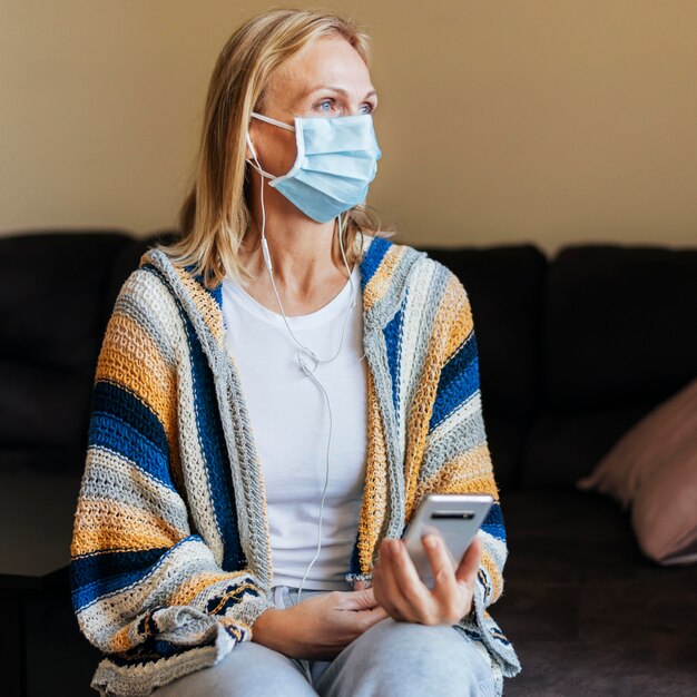 Donna a casa durante la quarantena con maschera medica e smartphone