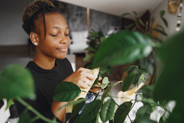 Woman at home. Girl in a black sweater. African woman use the rag. Person with flowerpot.