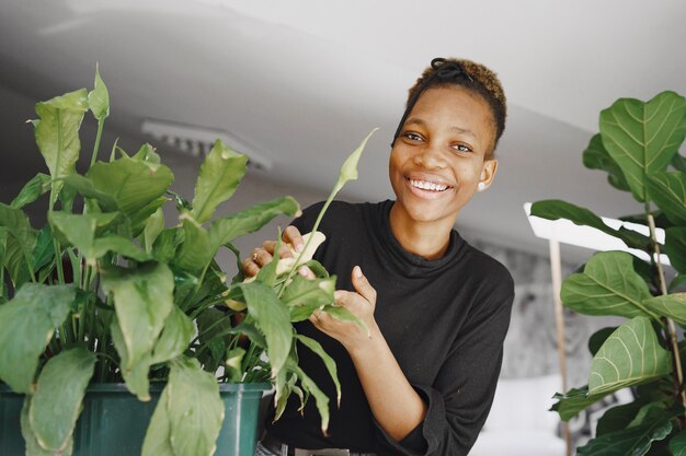 Woman at home. Girl in a black sweater. African woman use the rag. Person with flowerpot.