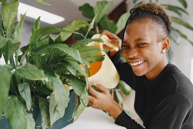 家にいる女性。黒のセーターを着た女の子。植物に水をまくアフリカの女性。植木鉢を持っている人。