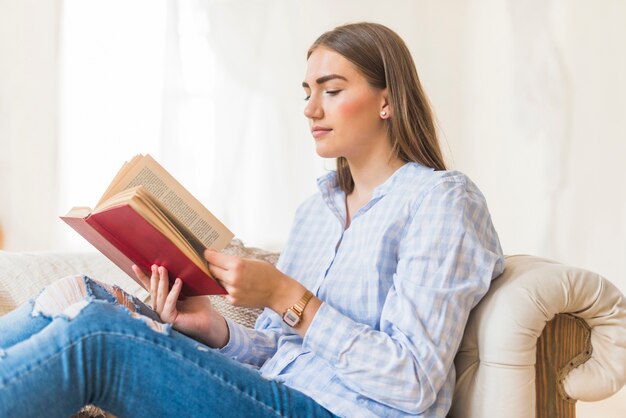 Woman at home on the sofa reading a book