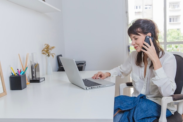 Foto gratuita donna a casa con il computer portatile a parlare al telefono