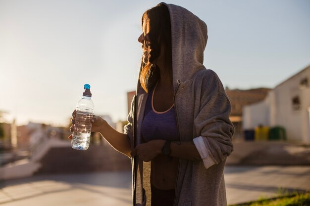 Woman in hoodie holding bottle with water