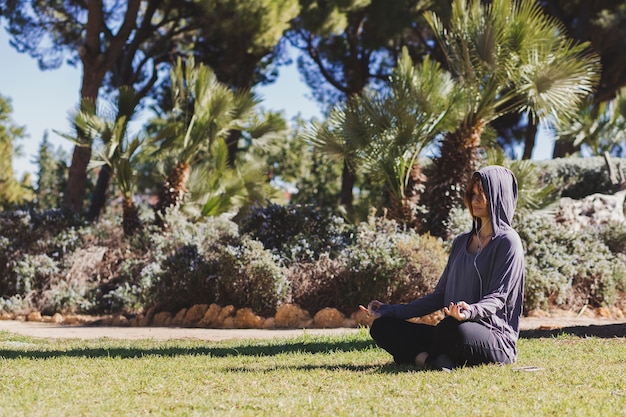 Woman in hoodie meditating in park