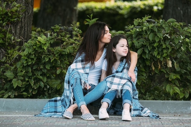 Woman hugging girl sitting on street curb