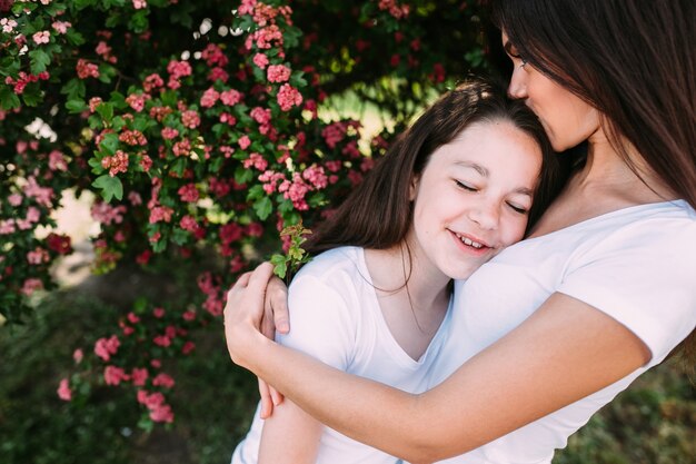 Woman hugging and kissing girl under tree