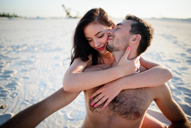 Woman hugs her man tender sitting on white sand