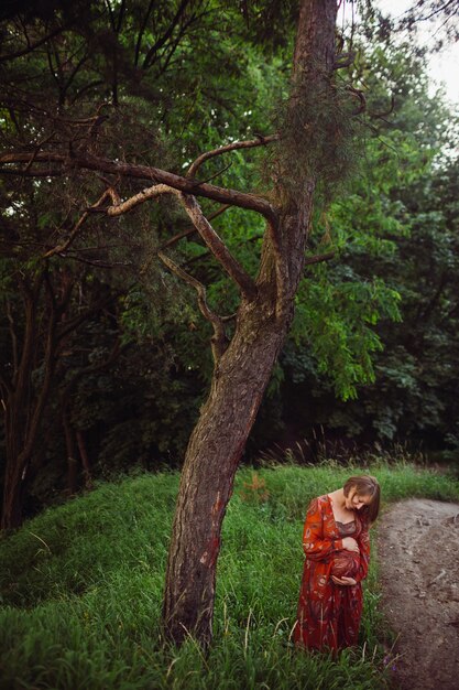 Woman hugs her pregnant belly posing in the forest 