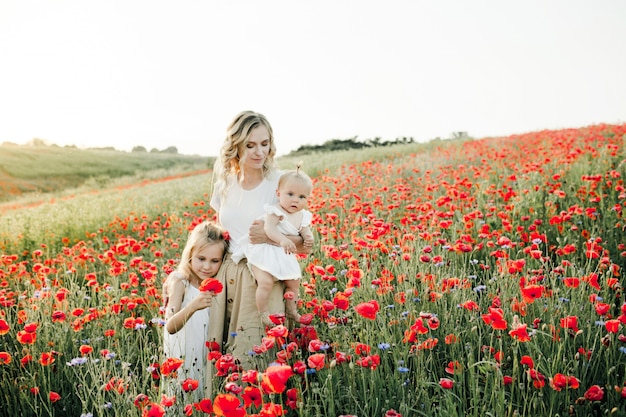 Woman hugs her two daughters among the poppy field