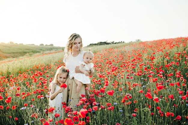 Woman hugs her two daughters among the poppy field