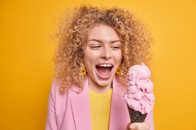 woman impressed by big size of ice cream keeps mouth widely opened looks at appetizing dessert wants to eat it immediately wears stylish clothes 