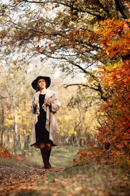 Женщина в платье и шляпе на фоне осенней листвы Premium Фотографии