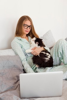 Женщина в пижаме держит кошку и работает из дома