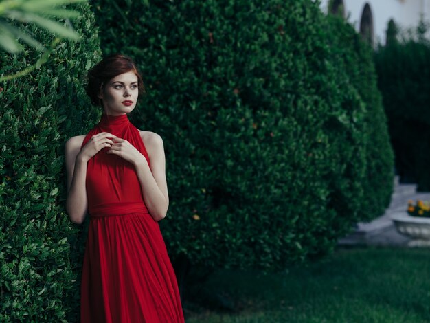 Женщина в красном платье гуляет в саду готической природы. фото высокого качества