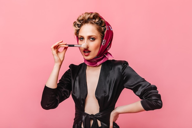 Бесплатное фото Женщина в шелковом халате и розовом шарфе держит кисть для макияжа и смотрит вперед