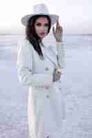 Бесплатное фото Женщина в белом женщины в зимней обуви европейская девушка в пальто улыбается в холодный день веселая светловолосая женщина веселится во время зимней фотосессии зимнее озеро над снегом теплые сапоги шляпа