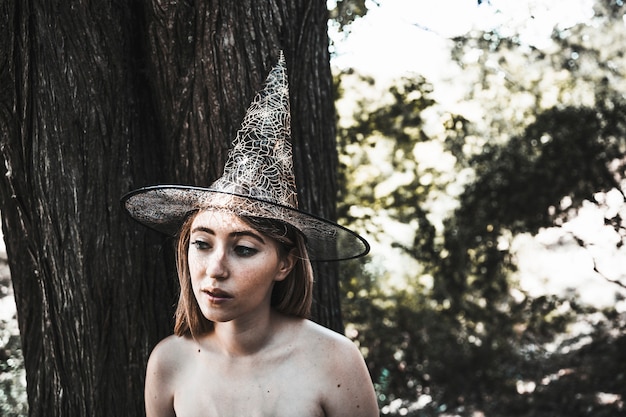 無料写真 木の近くに立っている魔女の帽子の女