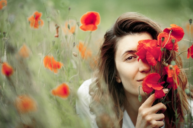 Woman is covering a face with a poppies flower bouquet