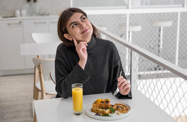 A woman is having breakfast with belgian waffles and orange juice