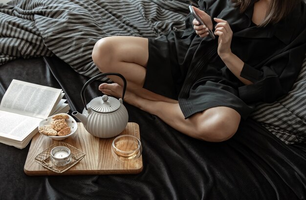 女性は休日にベッドに横たわって、お茶とクッキーで朝食をとっています。