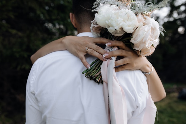 Foto gratuita la donna sta abbracciando l'uomo e sta tenendo il mazzo delle peonie bianche all'aperto, vista frontale dei dettagli