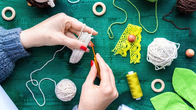 Woman is knitting using hooks and white yarn above the table with equipment