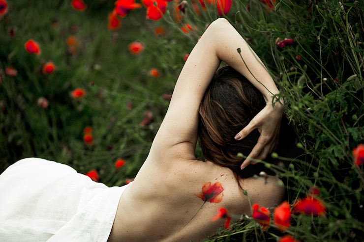 無料Photo 女性は裸の背中に横たわっており、入れ墨はケシの花の中で白いシャツに覆われています
