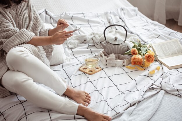 女性はお茶、本、チューリップの花束と一緒にベッドで休んでいます