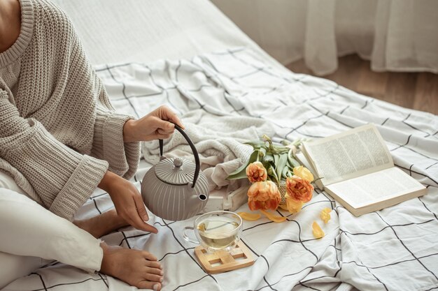Женщина отдыхает в постели с чаем, книгой и букетом тюльпанов.