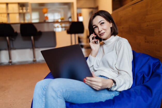 woman is sitting in blue bag chair working on laptop talking on phone