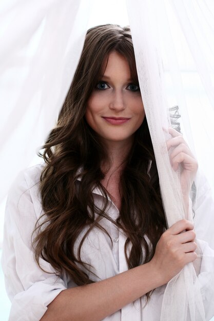 Woman is standing by the window playing with curtains