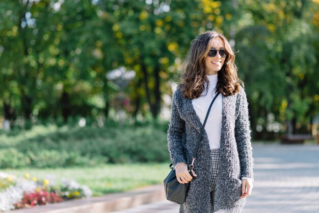 The woman is walking on the street with great smile. She has dark short hair and wonderful big blue eyes. She is dressed in grey pullover and white shirt.