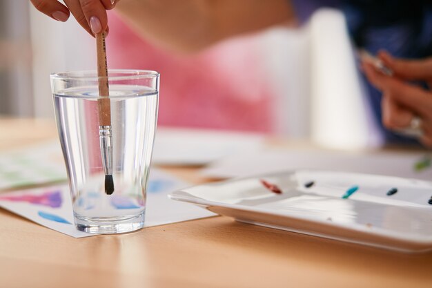 Woman is wetting the paintbrush in a glass with water