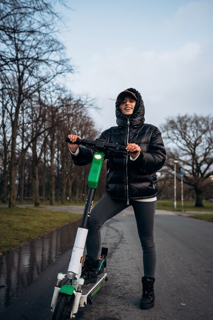 Woman in a jacket on an electric scooter in an autumn park.